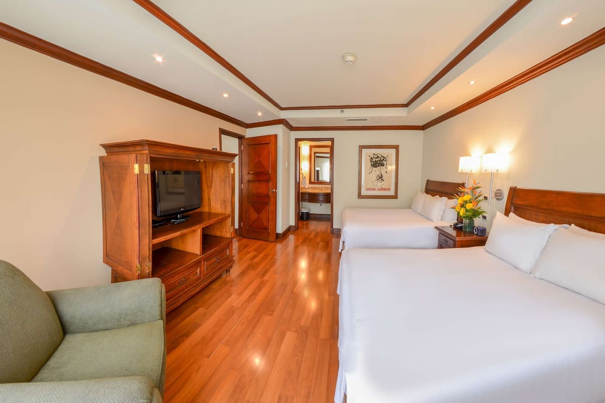 Habitación de hotel con dos camas, televisión, muebles de madera y un pasillo que conduce a un baño.