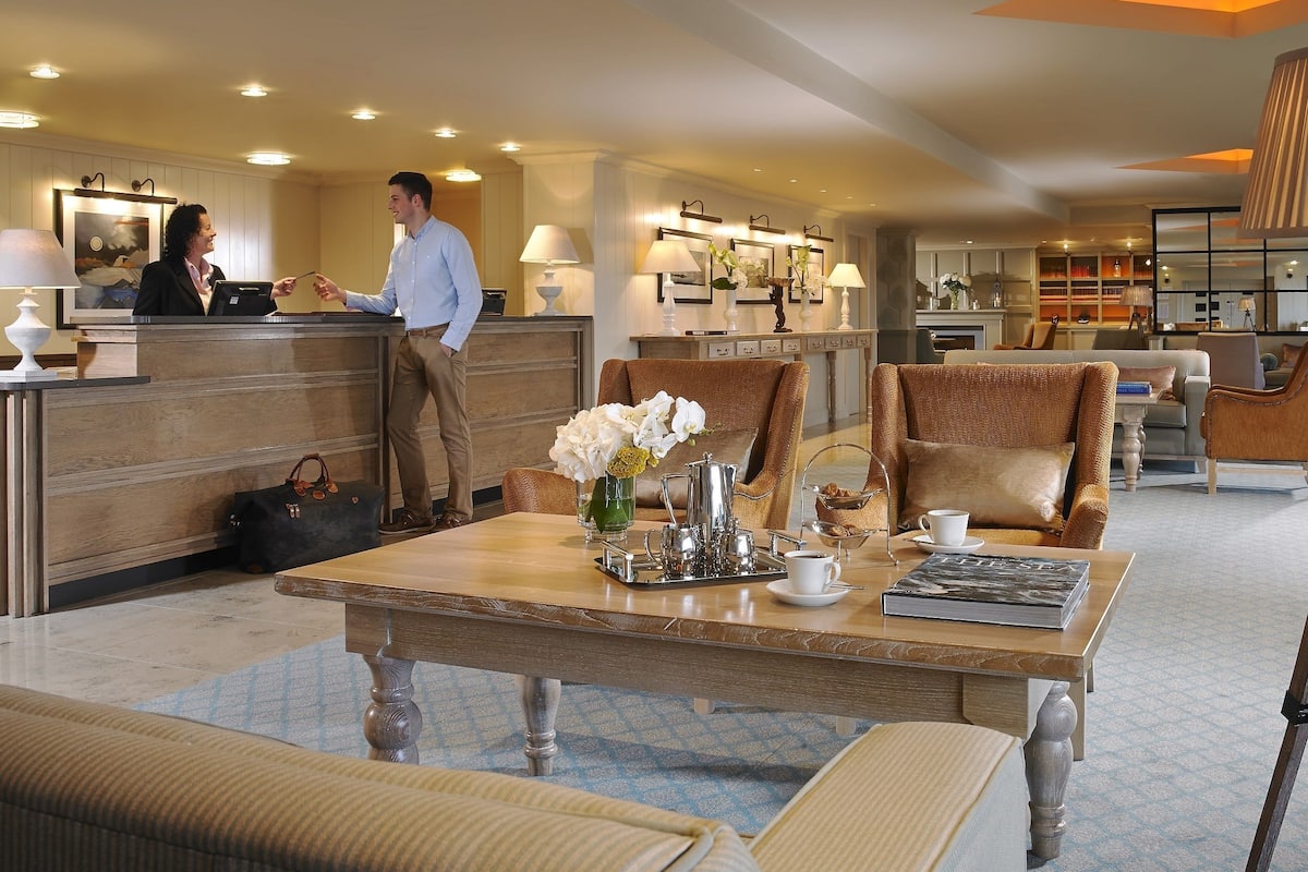 Vestíbulo de hotel con mostrador de recepción, zona de estar y una mesa de centro con detalles.