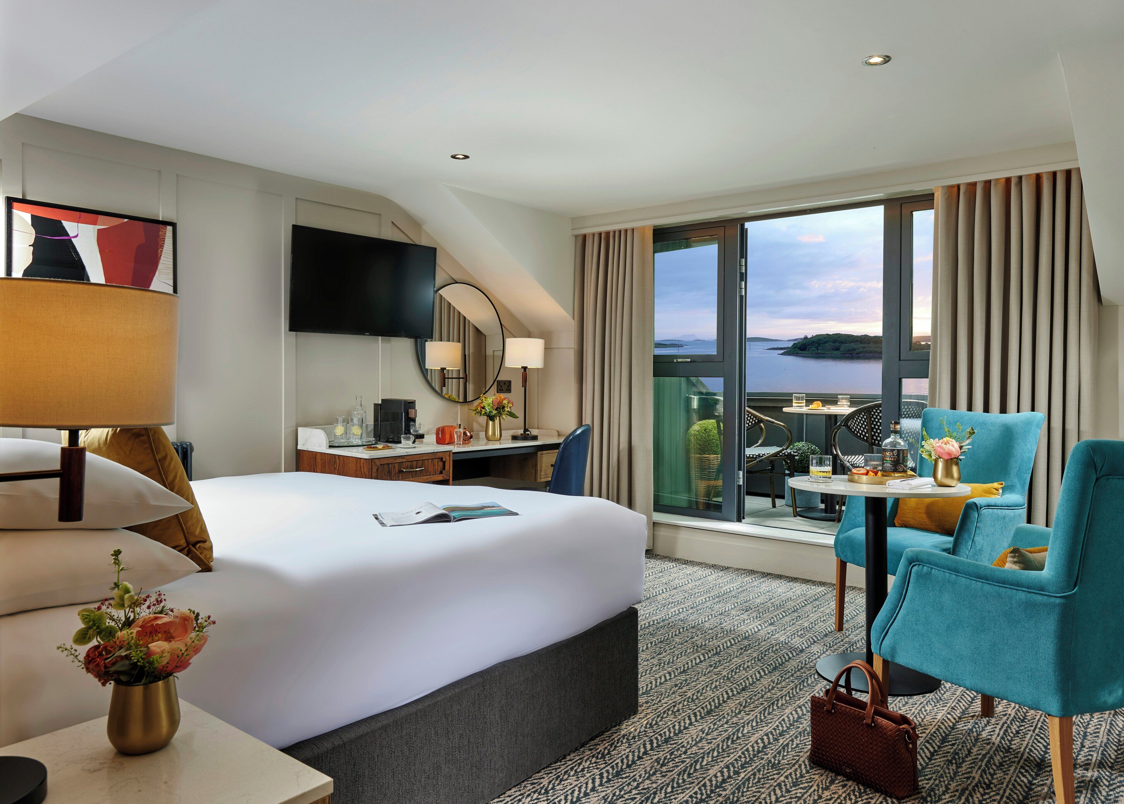 Habitación de hotel con una cama grande, un escritorio con computadora, un televisor y un balcón con vista al agua.