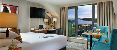 Habitación de hotel con una cama grande, un escritorio con computadora, un televisor y un balcón con vista al agua.