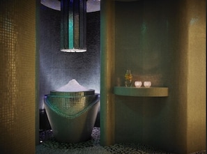 Zona de spa con una amplia cuenca texturizada, un estante con velas y una pared texturizada.