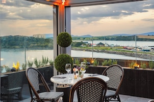 Una mesa para dos con vista a un río y edificios al fondo.