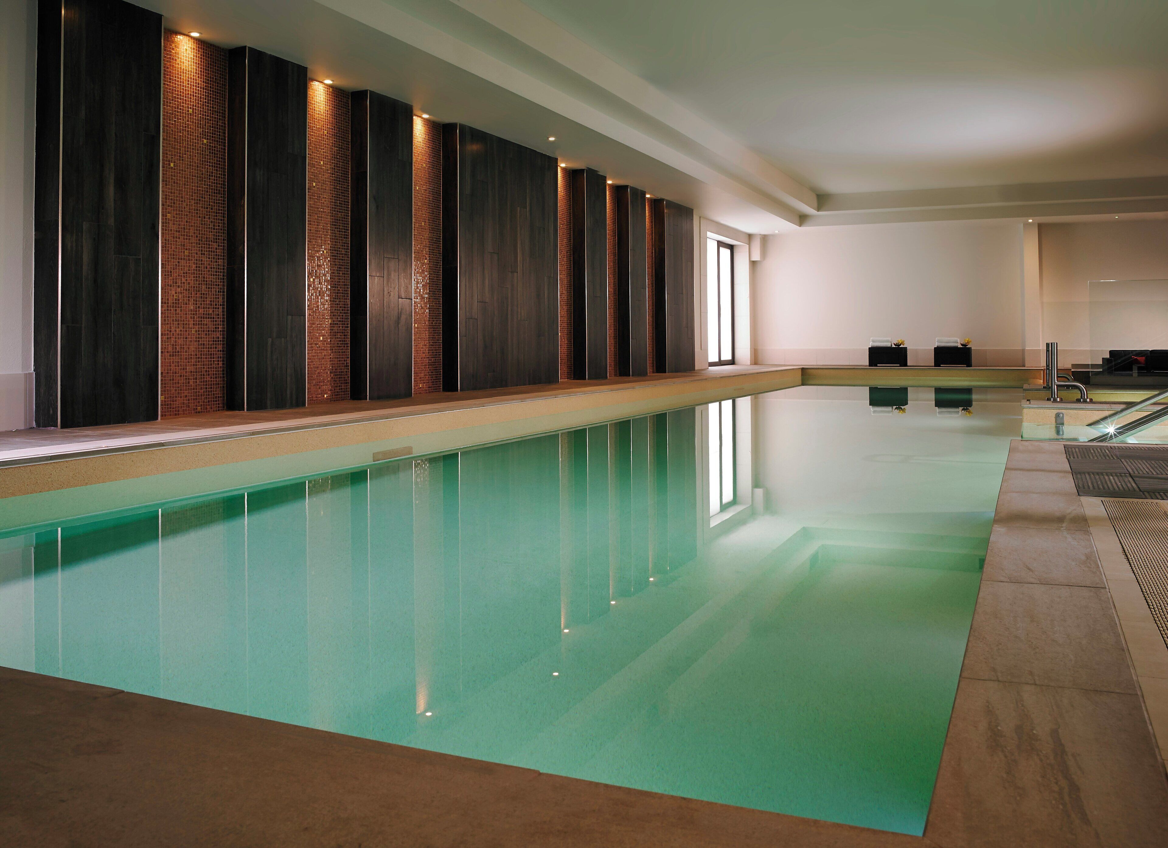 A long indoor swimming pool with a tiled wall and a wooden panel design on one side.
