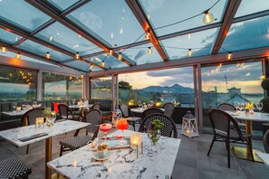 Un restaurante con terraza, amplias ventanas y luces colgantes.