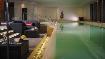 A modern indoor swimming pool area with a lounge area featuring sofas and a coffee table.