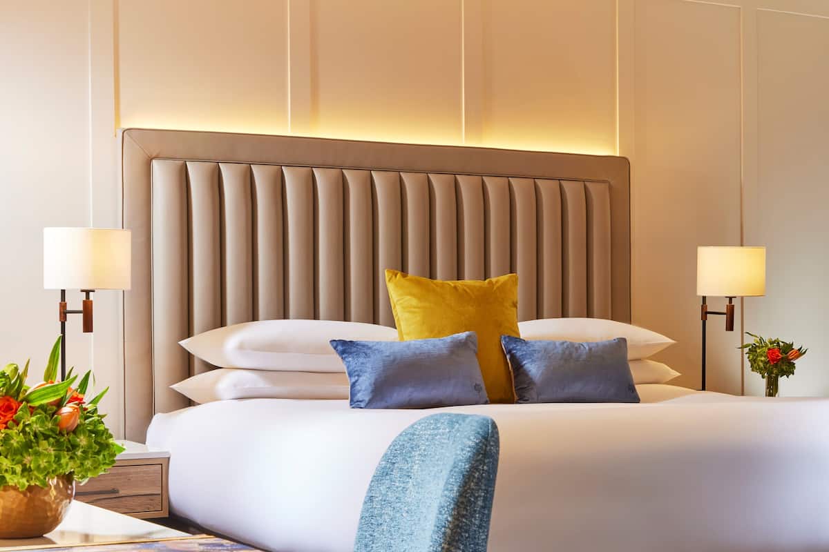 Habitación de hotel con una cama grande, dos lámparas de noche, un cabecero y una mesita de noche con una planta.