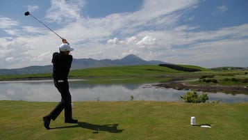 A golfer on a green with a lake and mountains in the background.