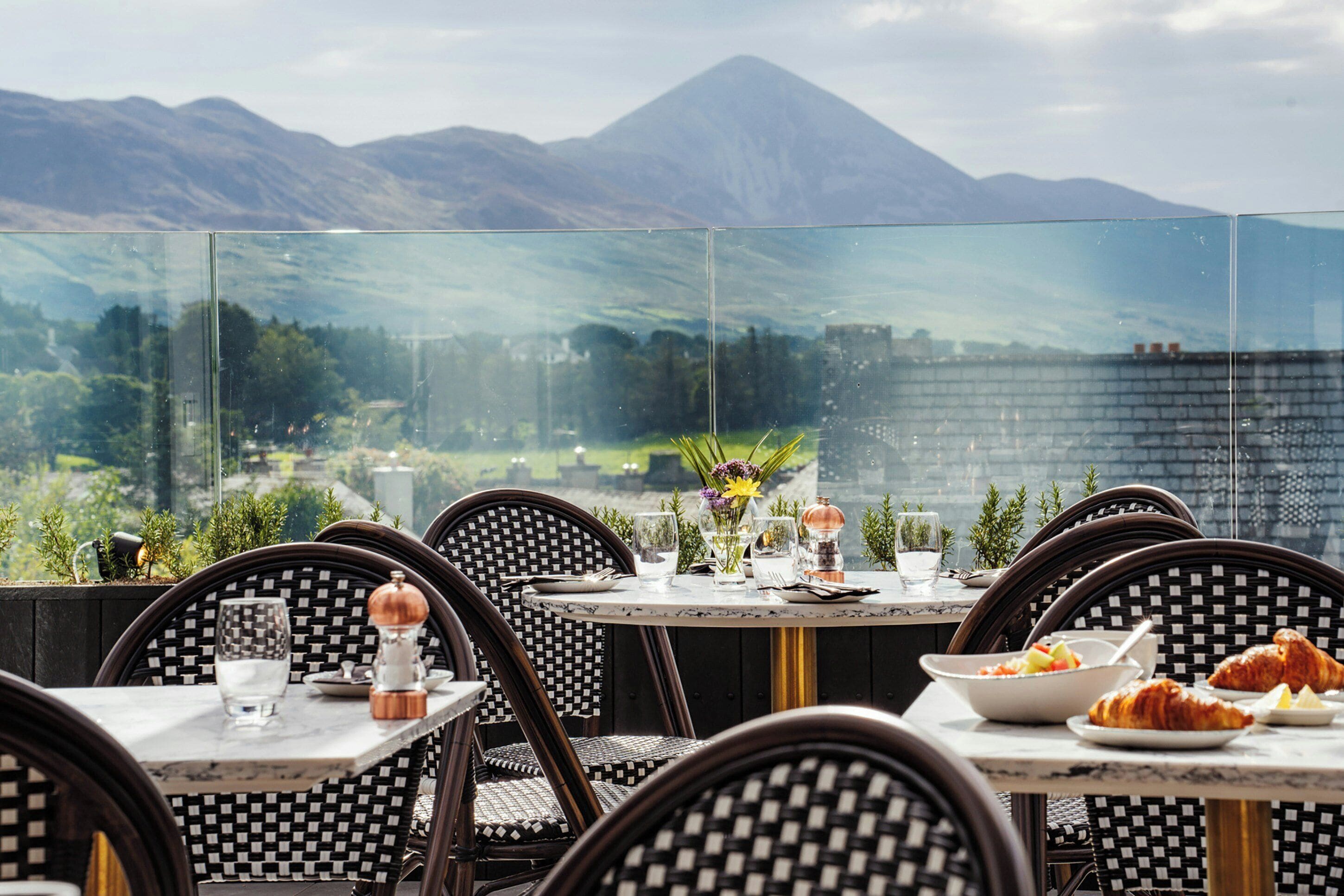 A dining area with tables and chairs, a view of mountains, and a glass wall.