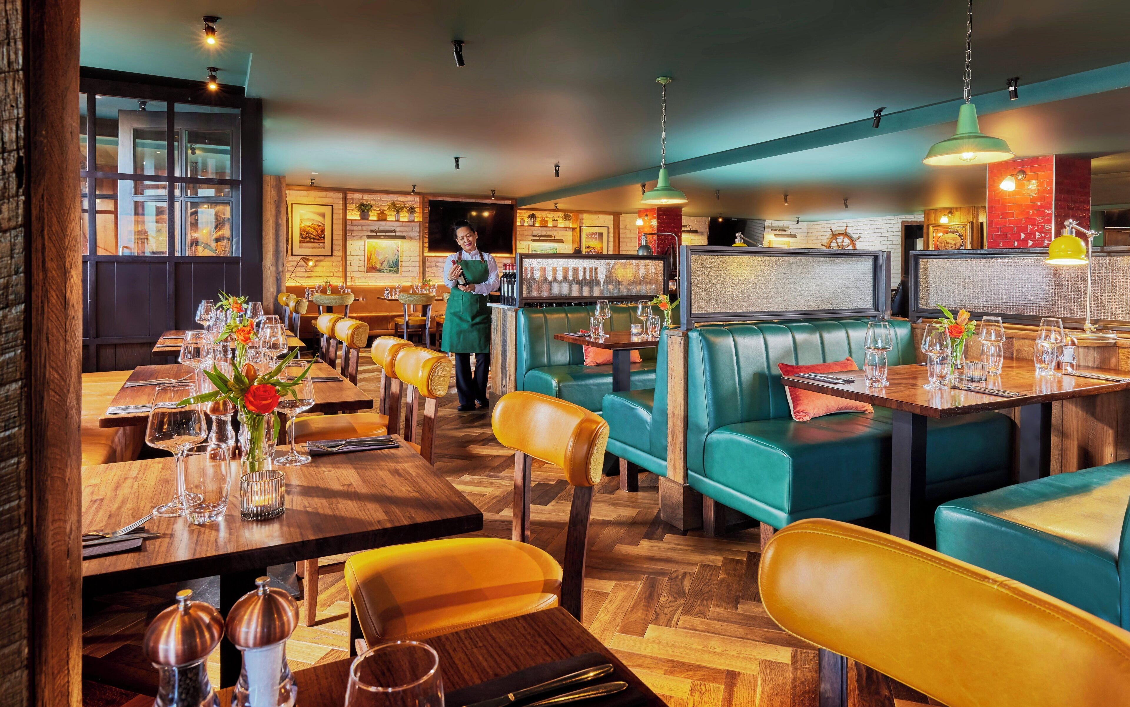 A restaurant with wooden tables, green upholstered booths, and a bar area.