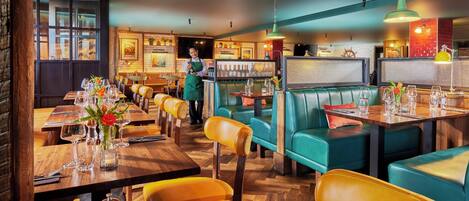 A restaurant with wooden tables, green upholstered booths, and a bar area.