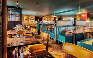Un restaurante con mesas de madera, asientos tapizados en verde y una zona de bar.