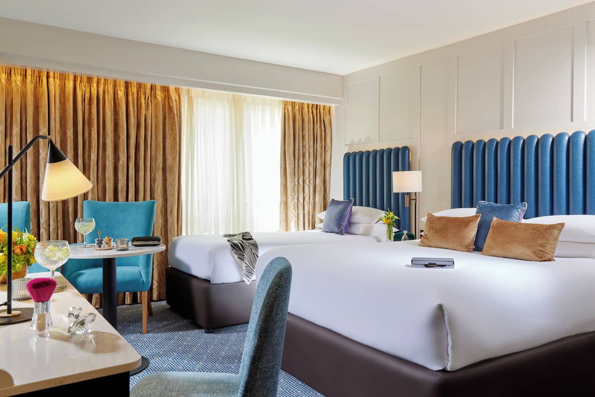Habitación de hotel con una cama grande, dos mesitas de noche, un escritorio con silla y una ventana con cortinas.