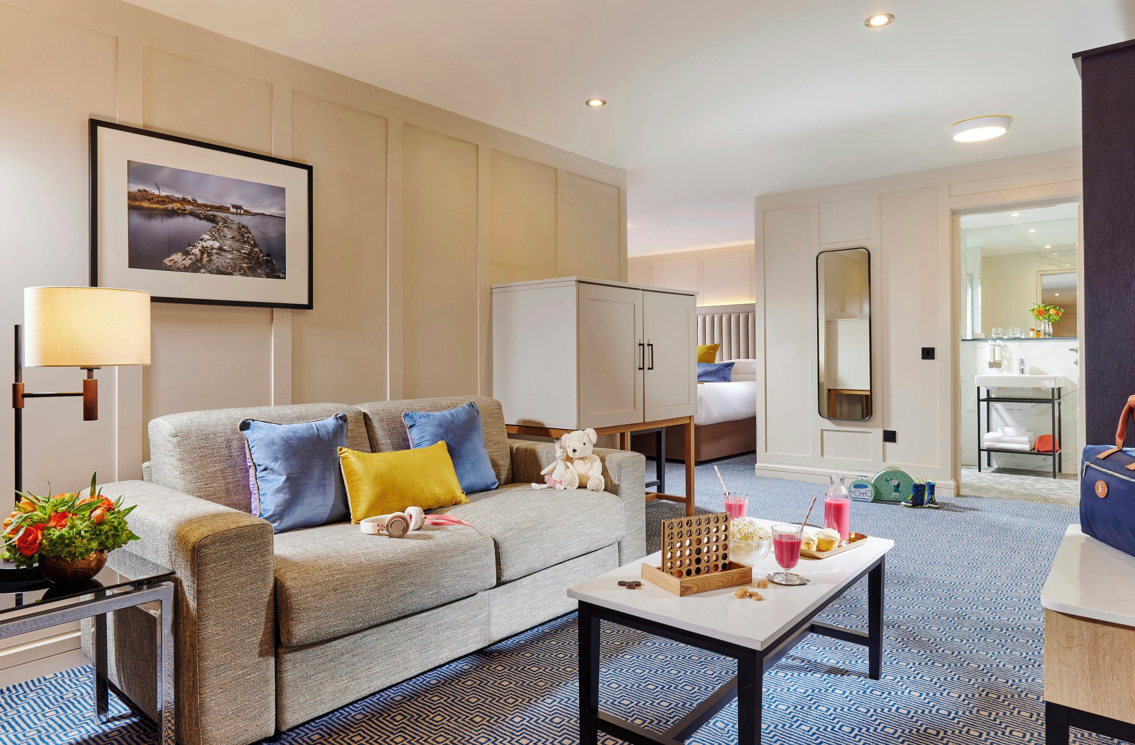 A hotel room with a sofa, a coffee table, a bed, a wardrobe, a bathroom with a mirror, and a framed picture on the wall.
