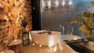 A modern bathroom with two freestanding tubs, a brick wall, and a large mirror.