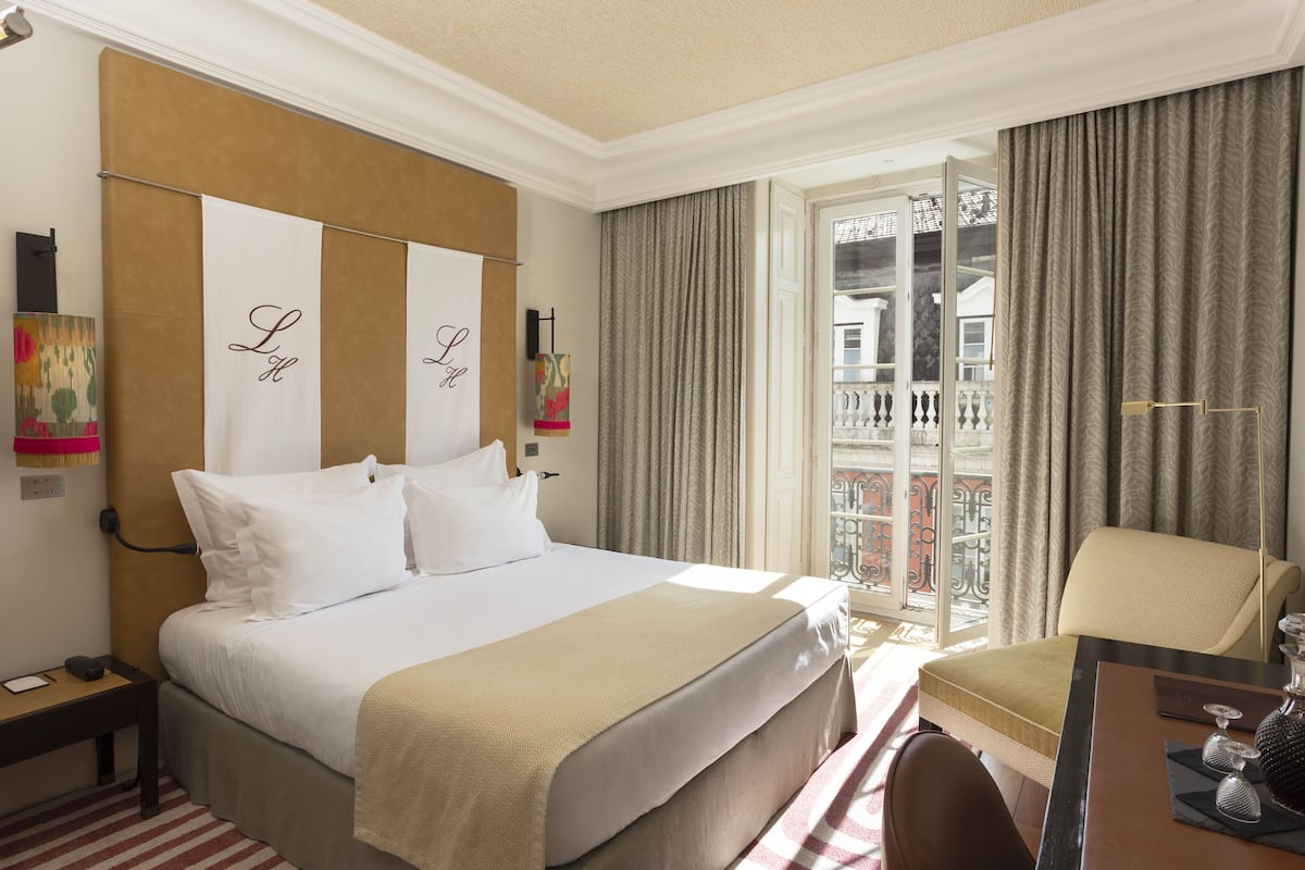 Een hotelkamer met een bed, een bureau, een stoel en een balkon met gordijnen.