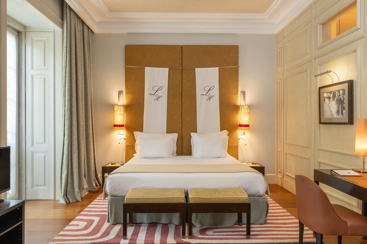 Een hotelkamer met een groot bed, twee nachtkastjes, een bureau, een stoel, een televisie en een ingelijst schilderij aan de muur.