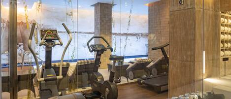 A gym with exercise equipment, a large window with a view, and a brick wall.