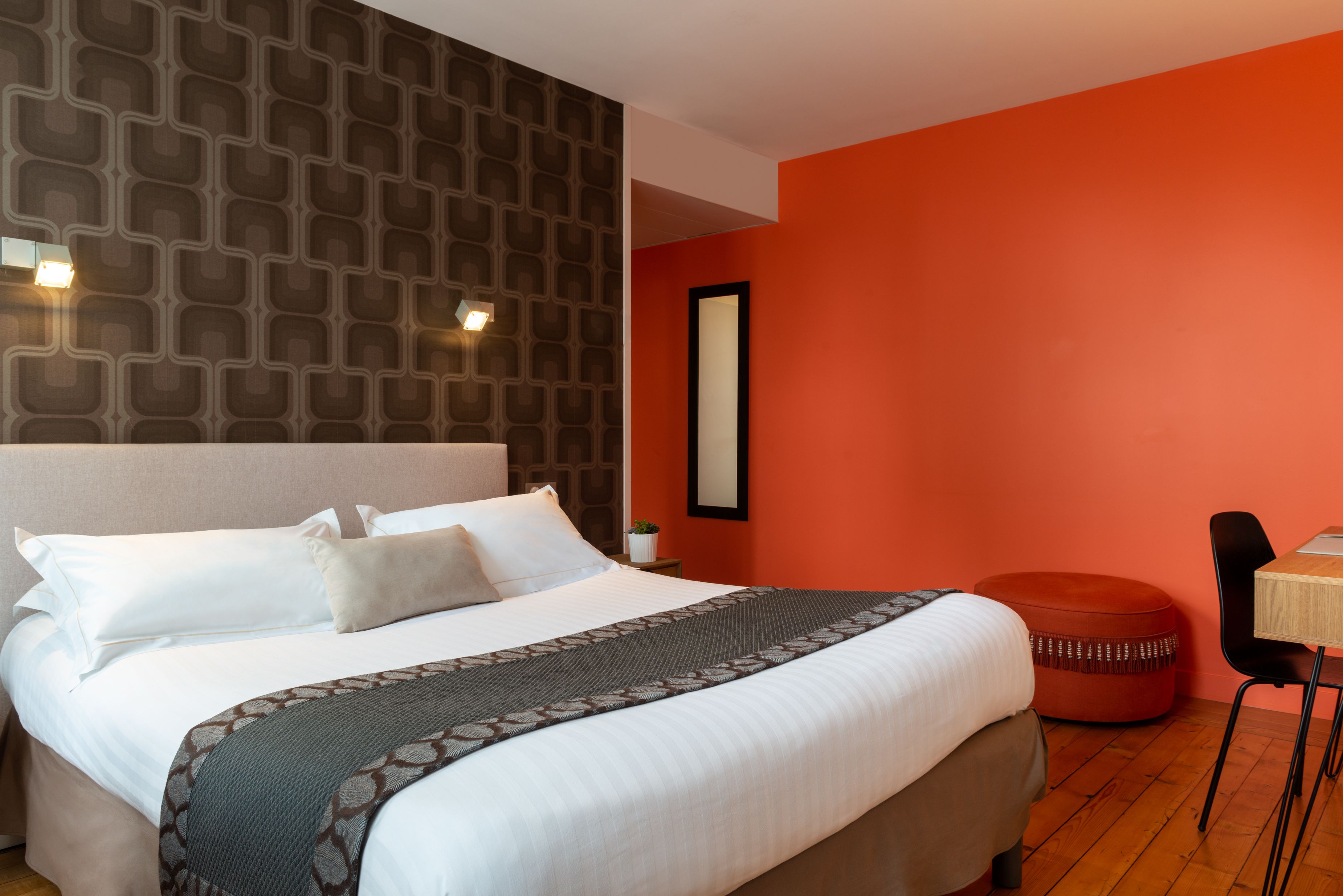 A hotel room with a large bed, a red accent wall, a small table, and a chair.