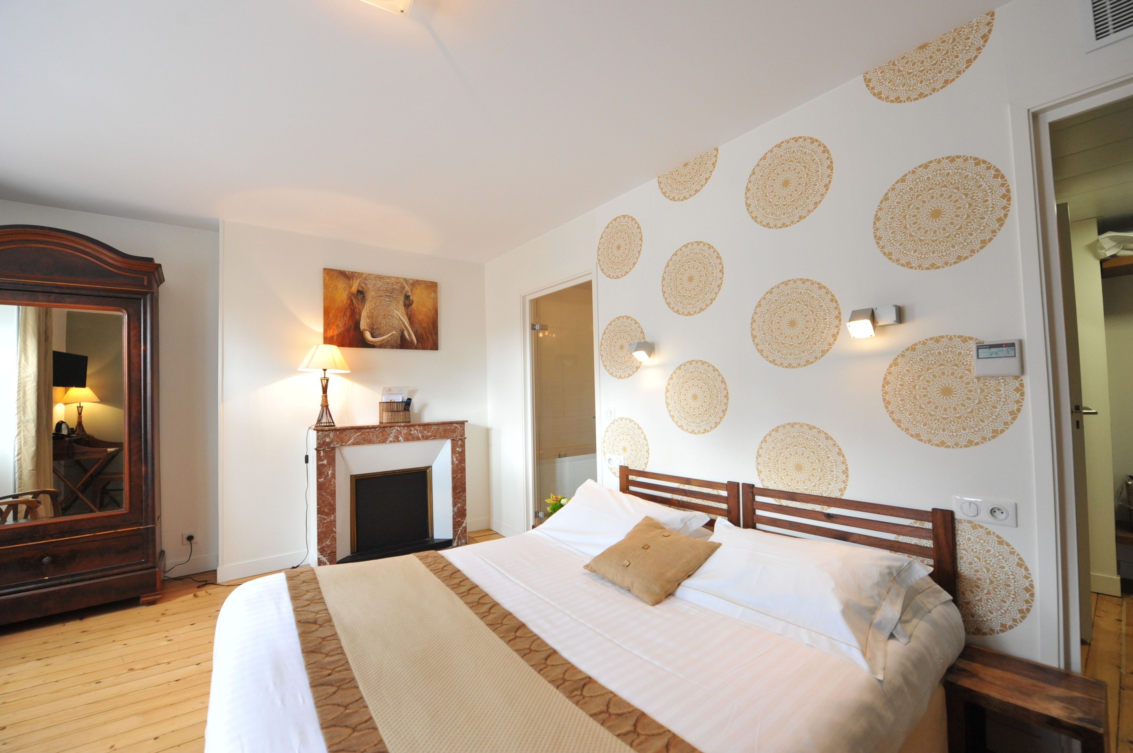 Un dormitorio con una cama grande, un aparador de madera, una chimenea y adornos de pared con motivos estampados.