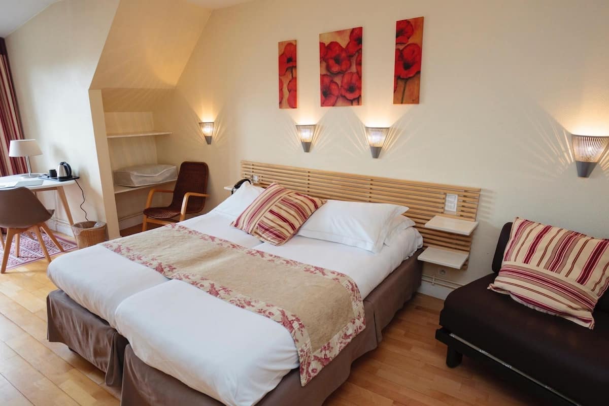 Une chambre d’hôtel avec un grand lit, un bureau, une chaise et un canapé. Il y a trois lampes fixées au mur et trois tableaux accrochés au mur.