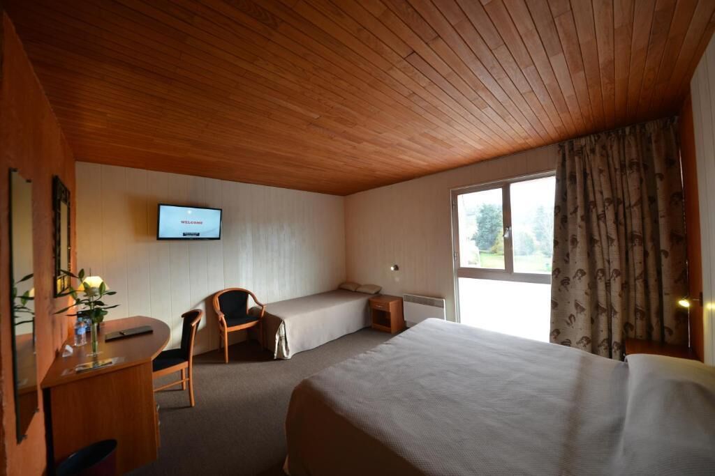 Une pièce avec un plafond en bois, un lit, un bureau avec une chaise, une petite table, un téléviseur et une fenêtre avec des rideaux.
