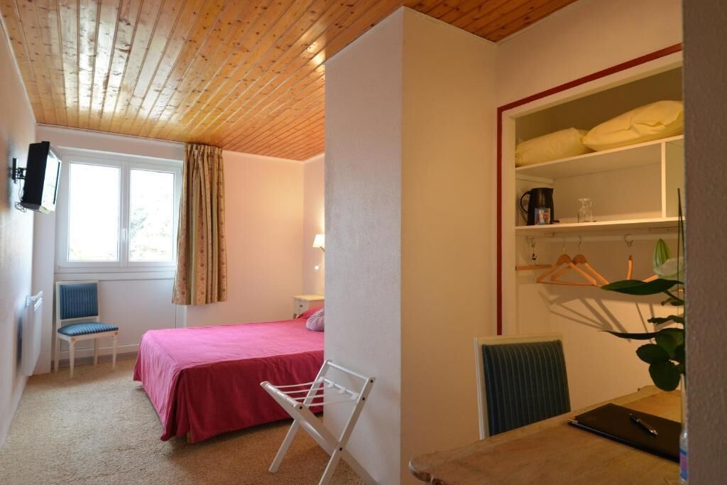 A bedroom with a bed, a chair, a drying rack, a desk with a chair, a radiator, and a window with curtains.
