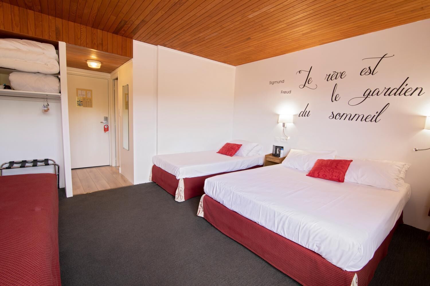 Habitación de hotel con dos camas, techo de madera y una pared con una cita en francés.