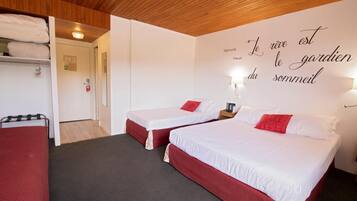 Habitación de hotel con dos camas, techo de madera y una pared con una cita en francés.