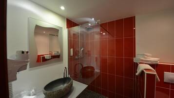 A modern bathroom with a large mirror, a stone basin, a glass shower enclosure, and red tiled walls.