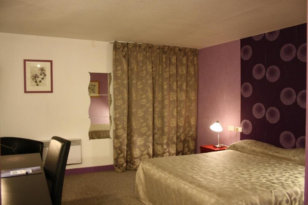 Ein Hotelzimmer mit Bett, Schreibtisch, Stuhl, Nachttisch mit Lampe und einer Wand mit einem kreisförmigen Muster.