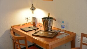 A wooden desk with a laptop, a bottle of water, a wine glass, and a bottle of champagne.