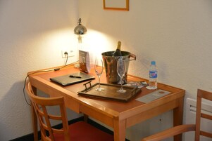 Uma mesa de madeira com um laptop, uma garrafa de água, uma taça de vinho e uma garrafa de champanhe.
