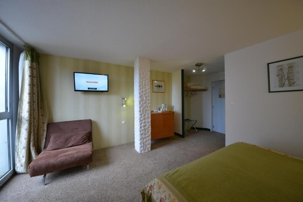 A hotel room with a bed, a sofa, a television, and a bathroom visible in the background.
