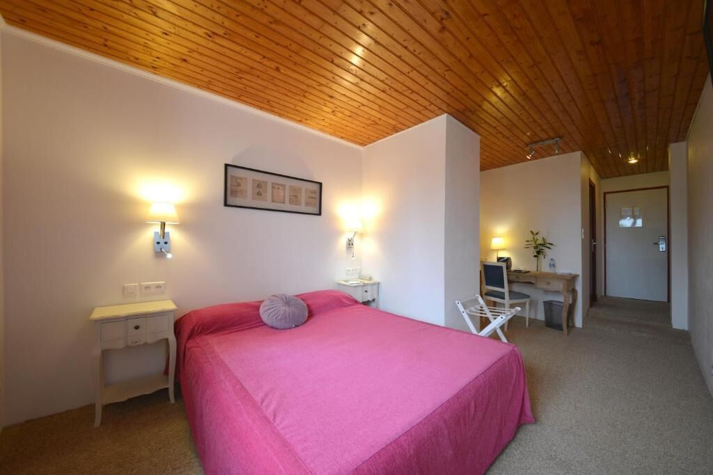 Ein Schlafzimmer mit Holzbalkendecke, einem Bett mit rosa Bettwäsche, Nachttischen mit Lampen und einem Schreibtisch mit Stuhl.