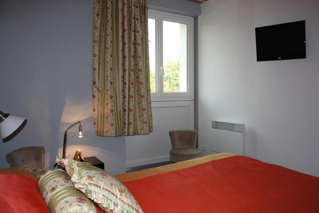 Ein Schlafzimmer mit Bett, Schreibtisch, Stuhl, einem Fenster mit Vorhängen, einem an der Wand befestigten Fernseher und einer Heizung.