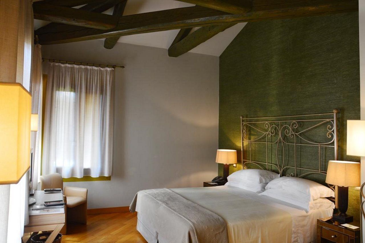 A hotel room with a bed, two bedside tables with lamps, a chair, a desk, and a window with curtains.