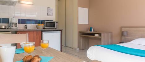 A hotel room with a bed, a bedside table with a lamp, a small kitchenette with a microwave, a coffee maker, and a refrigerator.