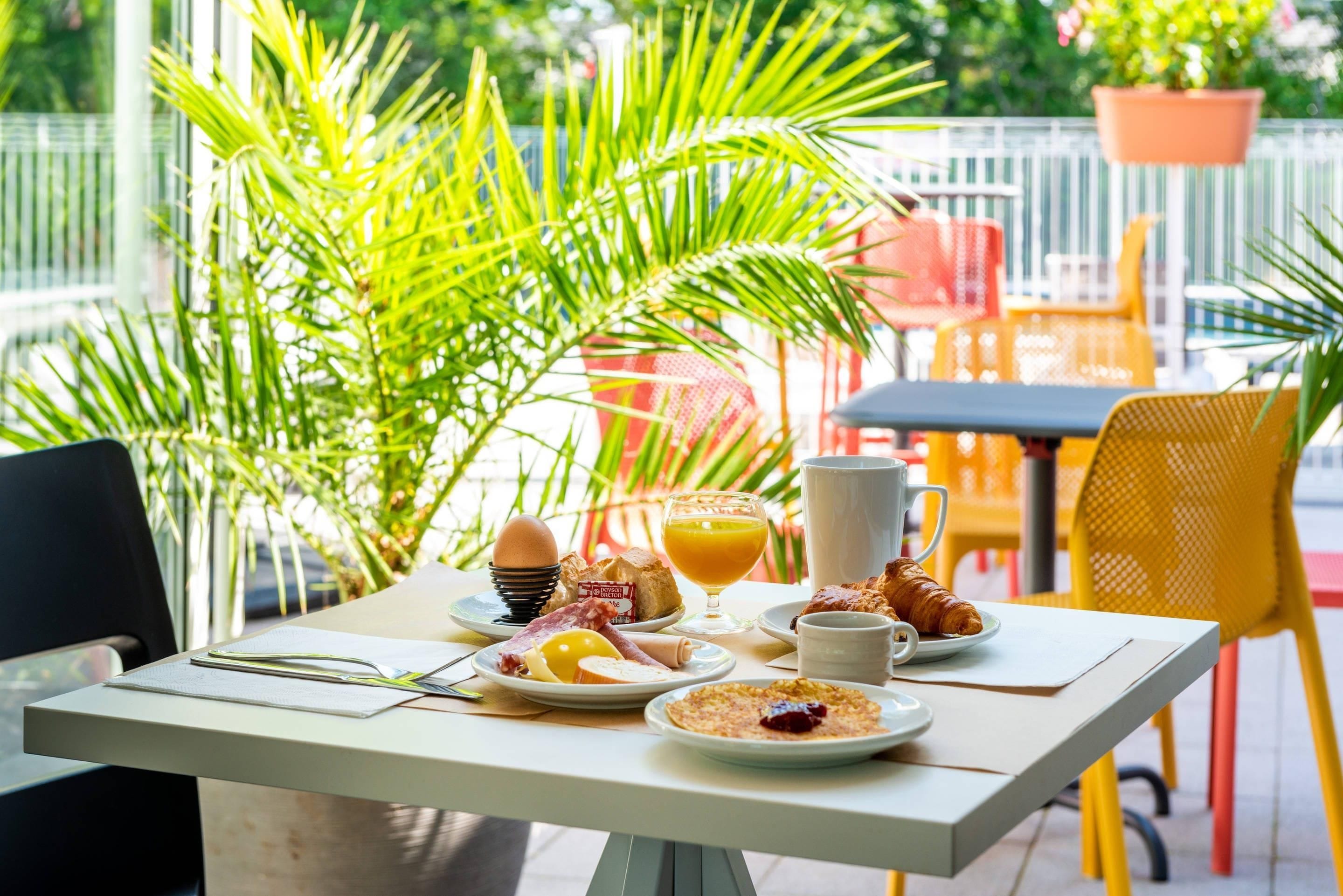 A breakfast table with plates of food, a glass of orange juice, and a croissant.