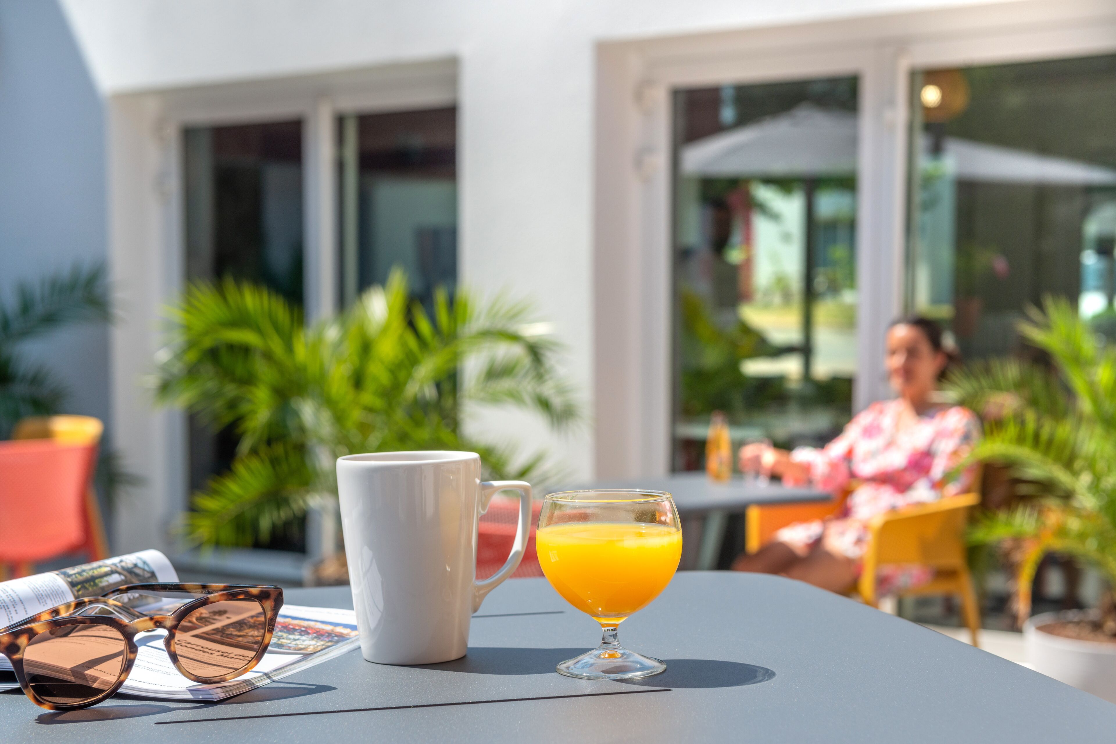 A table with a white mug, a clear glass of orange juice, and a pair of sunglasses.