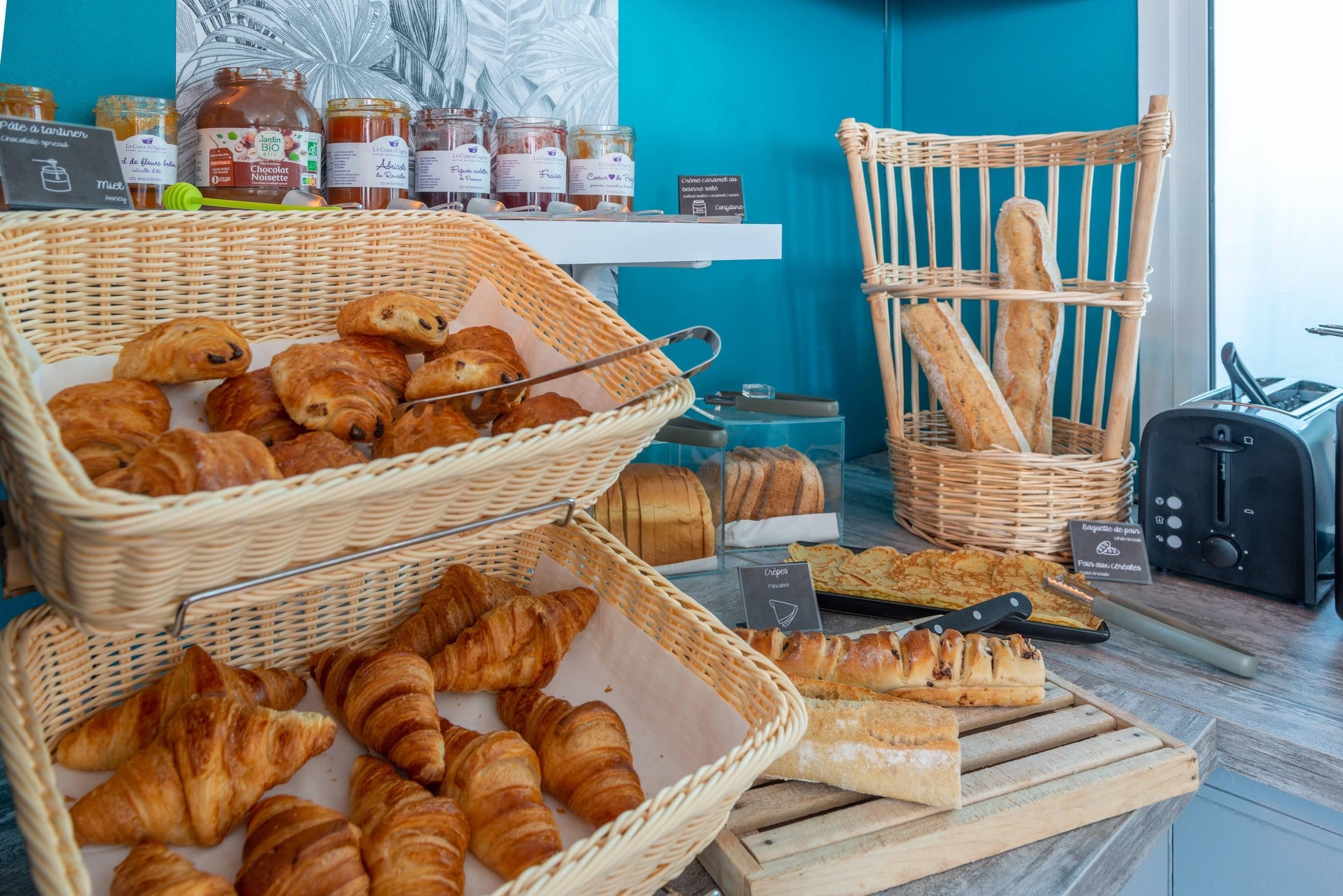 Une vitrine de boulangerie avec des paniers remplis de croissants et de baguettes, des pots de miel et un grille-pain.