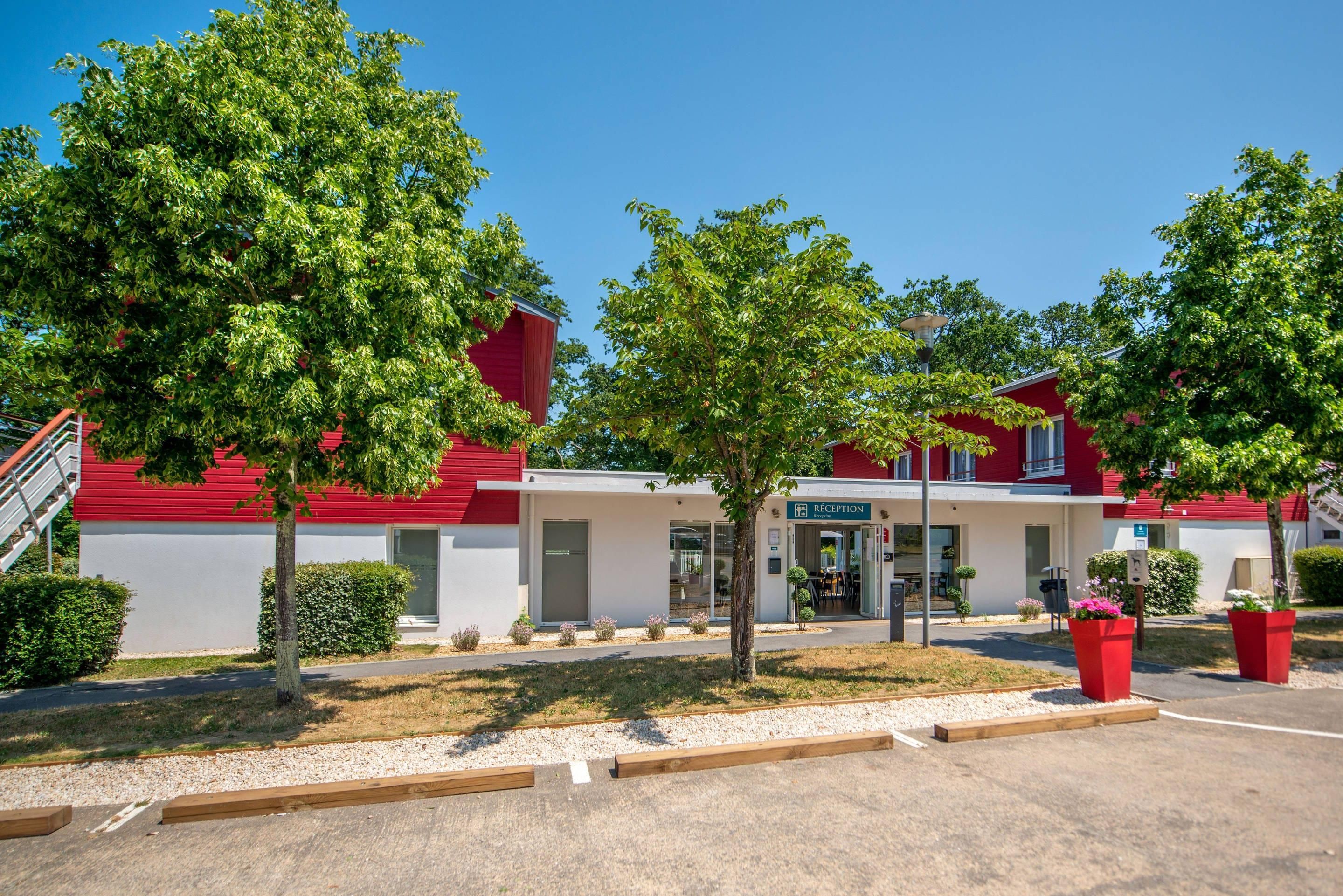 A red and white building with a reception area, trees, and a parking lot.