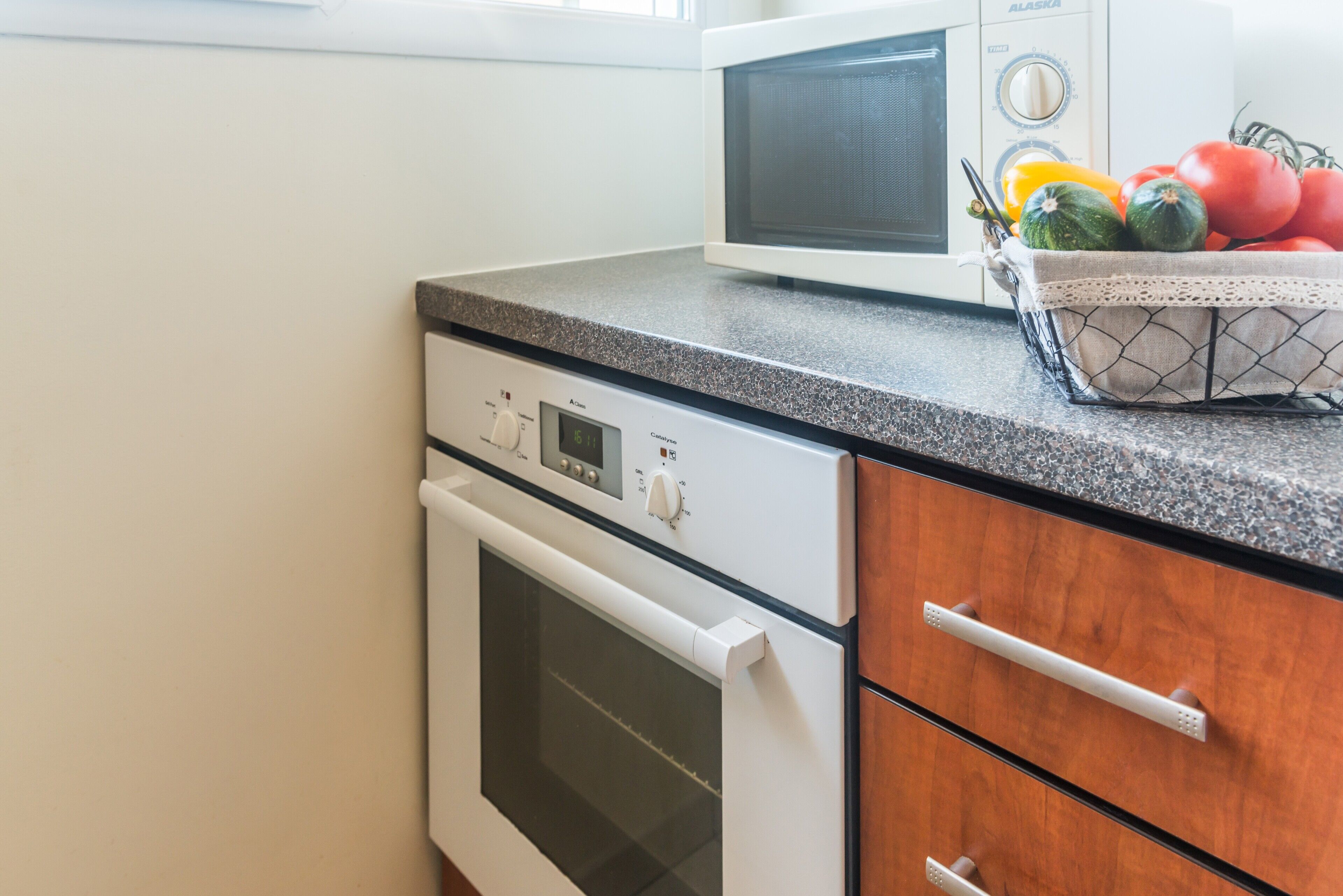 A kitchen with a white oven, a microwave, and a fruit basket on the counter.