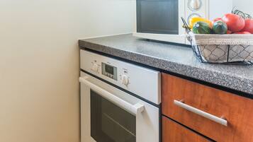 A kitchen with a white oven, a microwave, and a fruit basket on the counter.