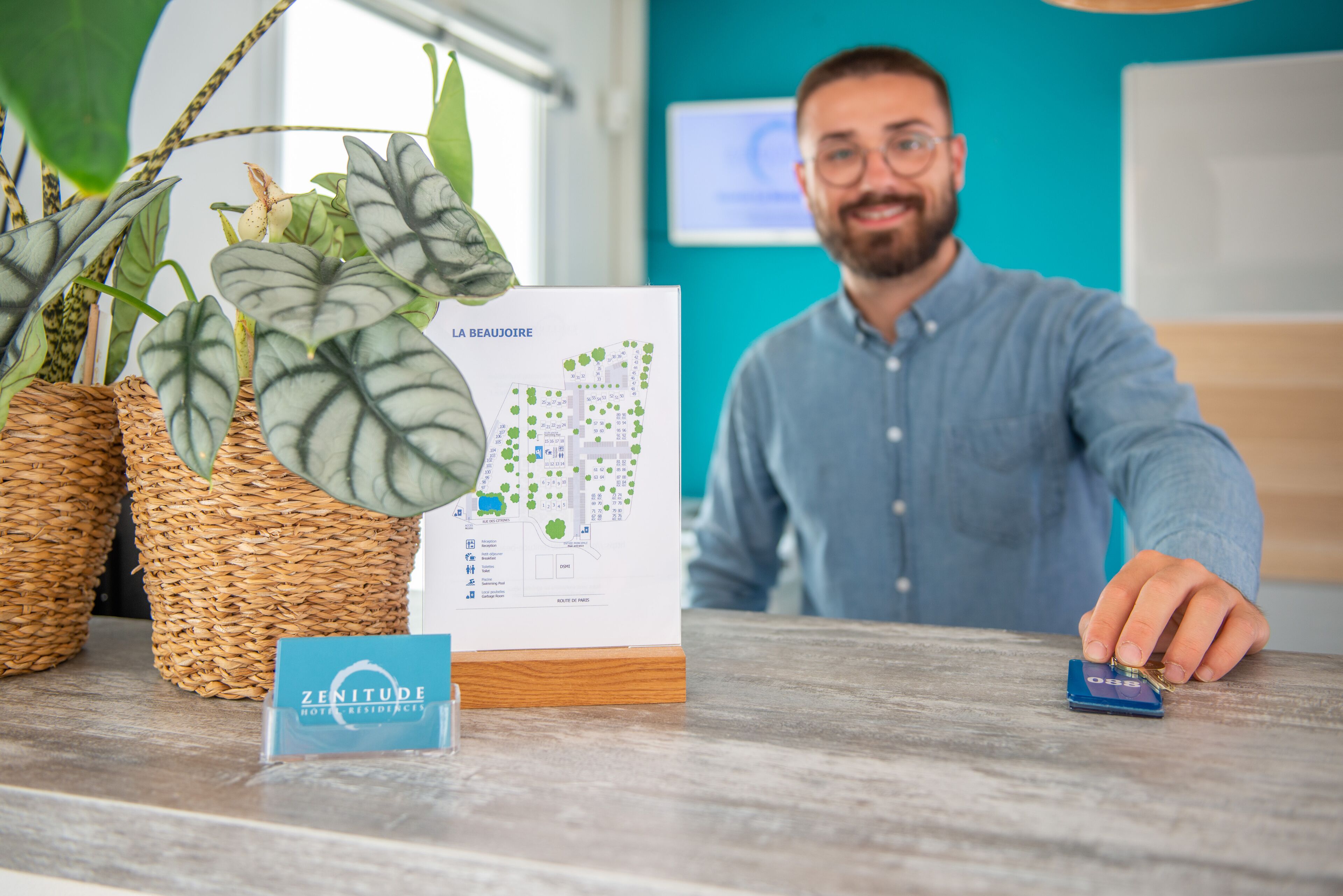 A reception desk with a map, a sign for 'ZENITUDE HOTELS & RESORTS', and a potted plant.