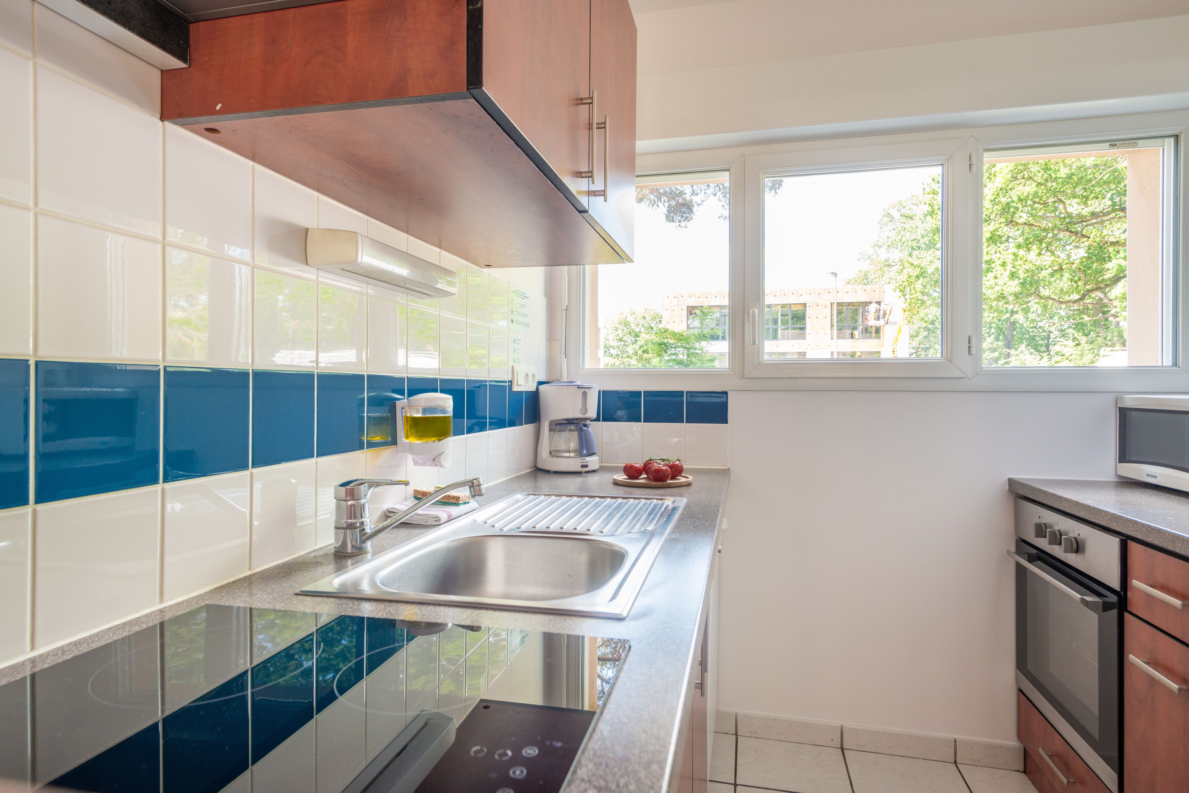 A modern kitchen with a stainless steel sink, a built-in oven, and a window providing natural light.