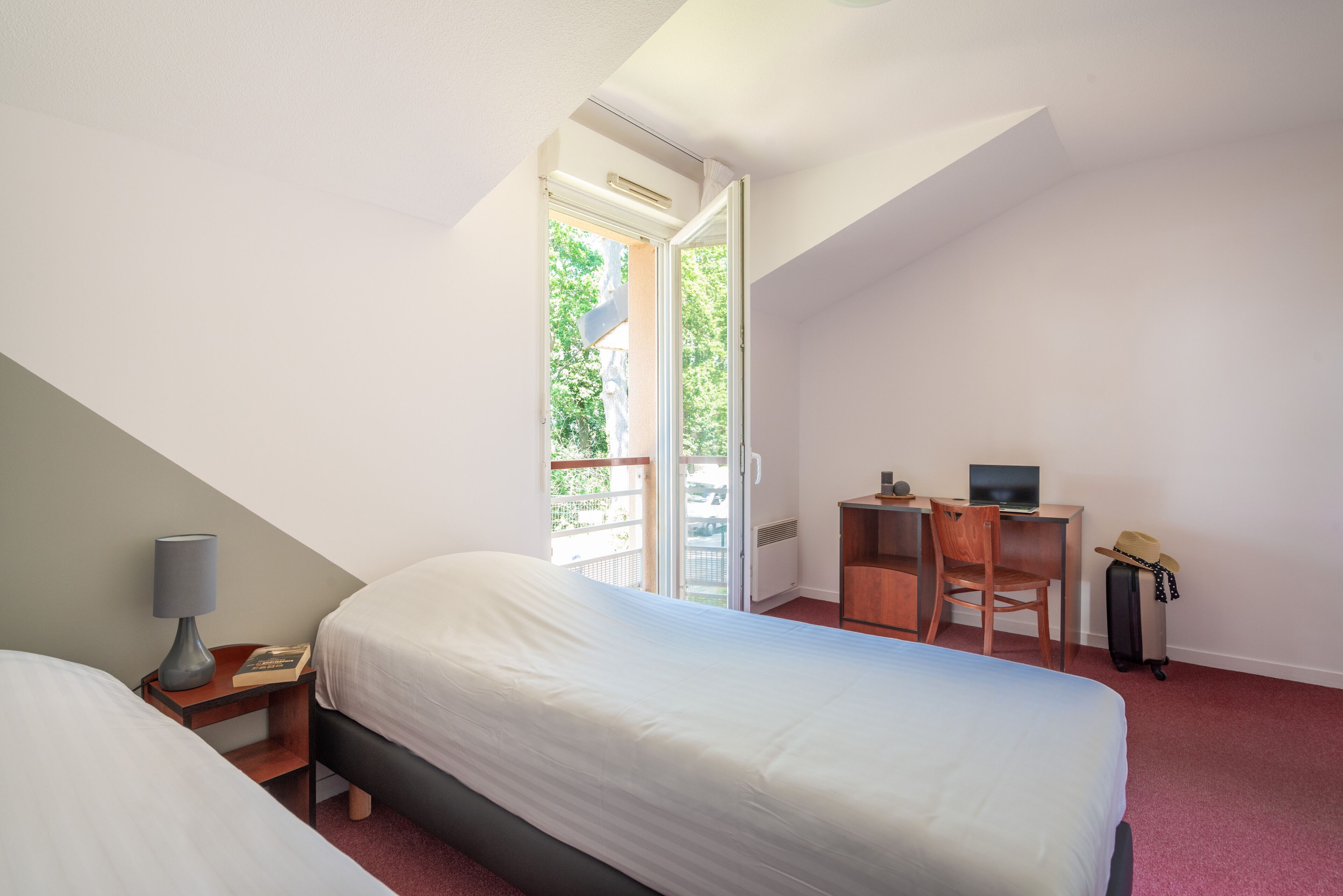 Ein Hotelzimmer mit Bett, Schreibtisch, Stuhl, Lampe und Koffer.