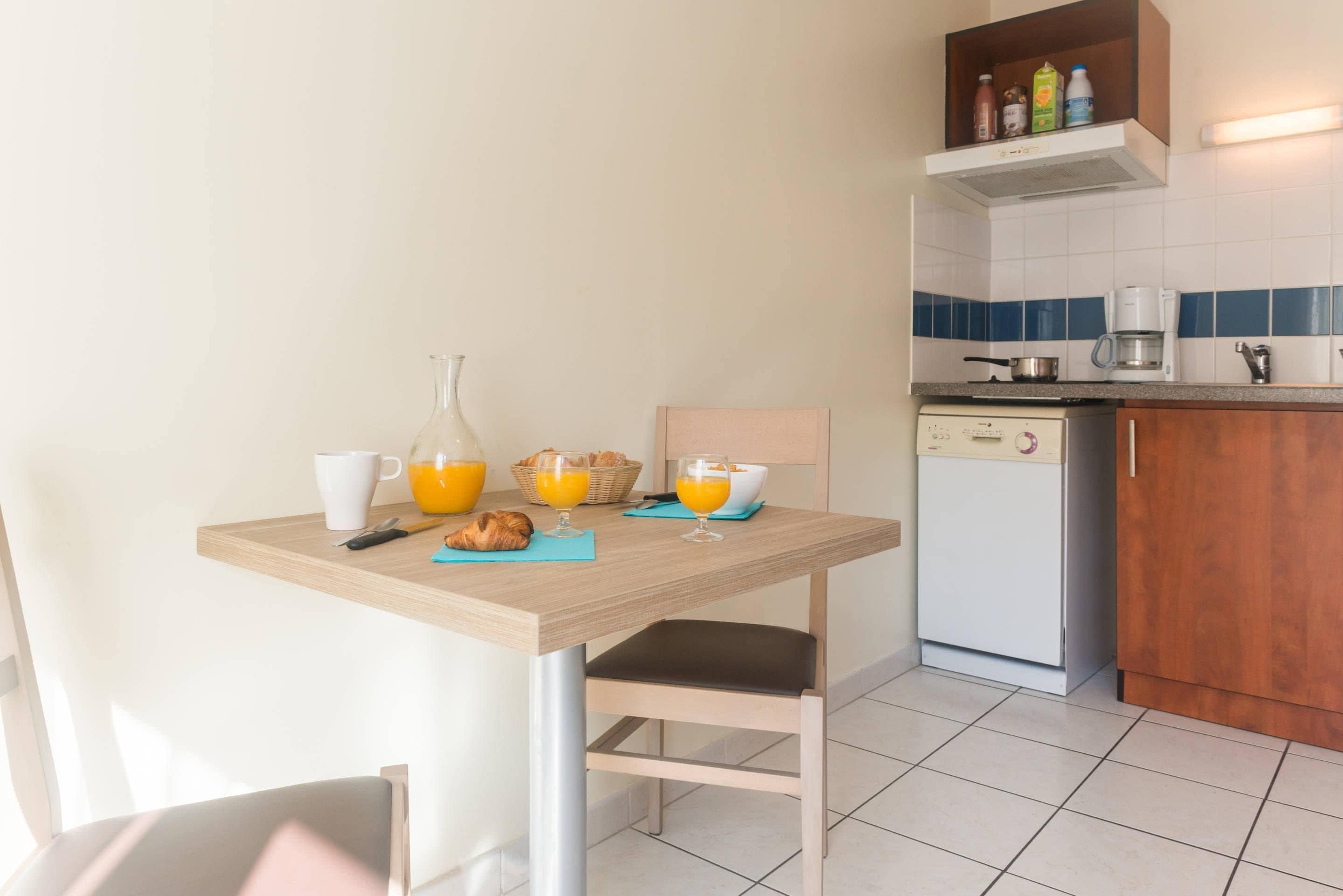 Una cocina con mesa, sillas, cafetera y lavavajillas.