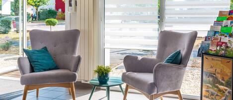 A modern interior with two grey armchairs, a small round table with a plant, and a window with blinds.