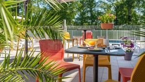 An outdoor patio with a table set for breakfast, surrounded by chairs and potted plants. - Comfort Aparthotel Nantes La Beaujoire (Nantes)