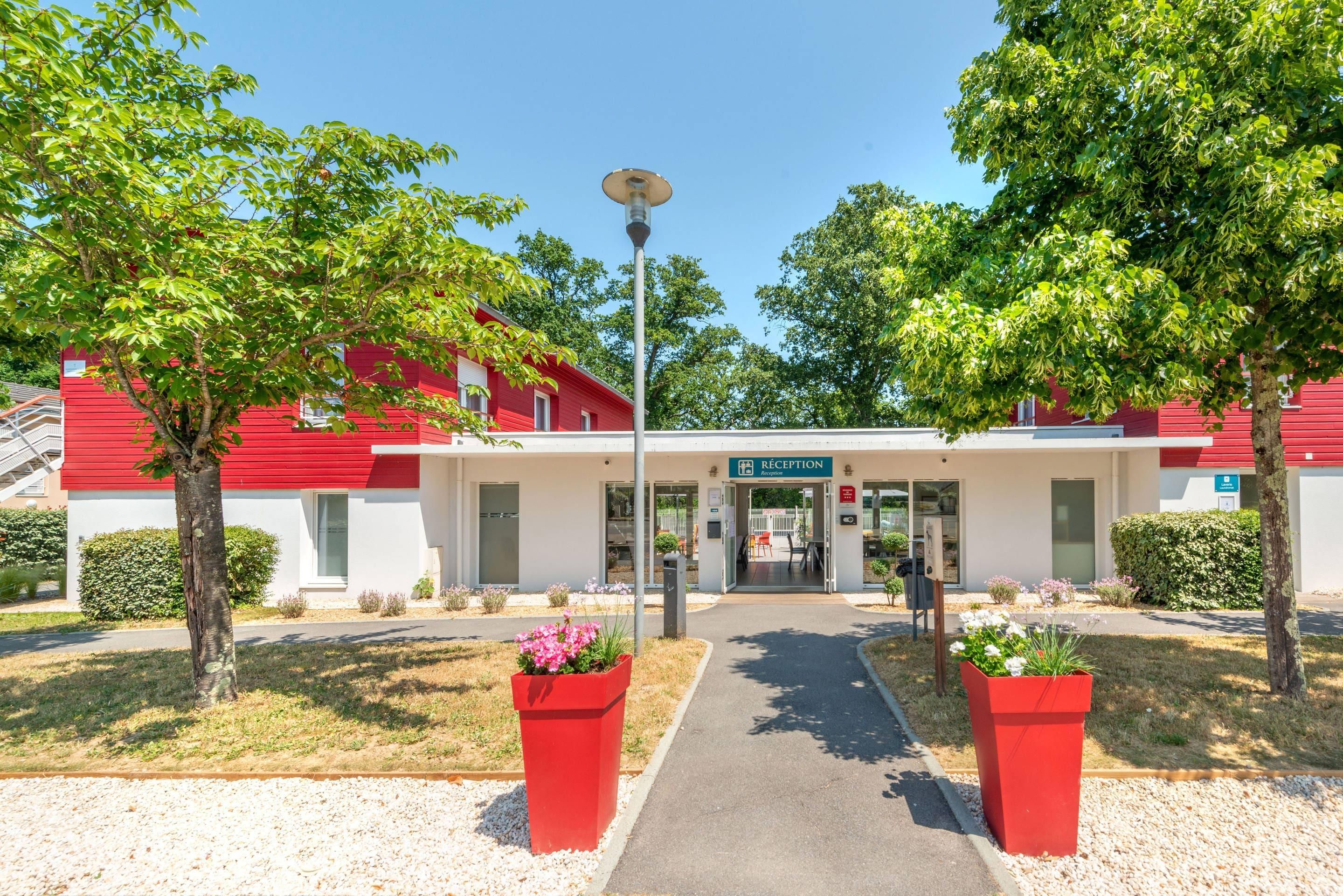 A building with a reception area, a pathway leading to it, and red planters with flowers.